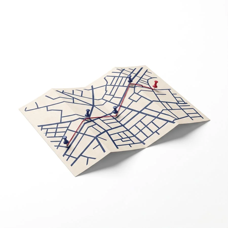 A folded paper map with a red thread route linking navy push pins.